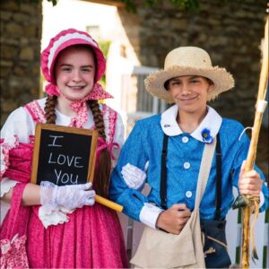 Natalie Vandiver as Becky Thatcher on the left in a pink patterned dress. Kael Viehmann as Tom Sawyer on the right in a blue patterned shirt